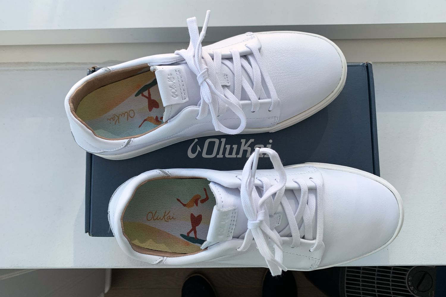 Olukai Pehuea Lī ‘Ili Women’s Leather Sneakers displayed on top of their box