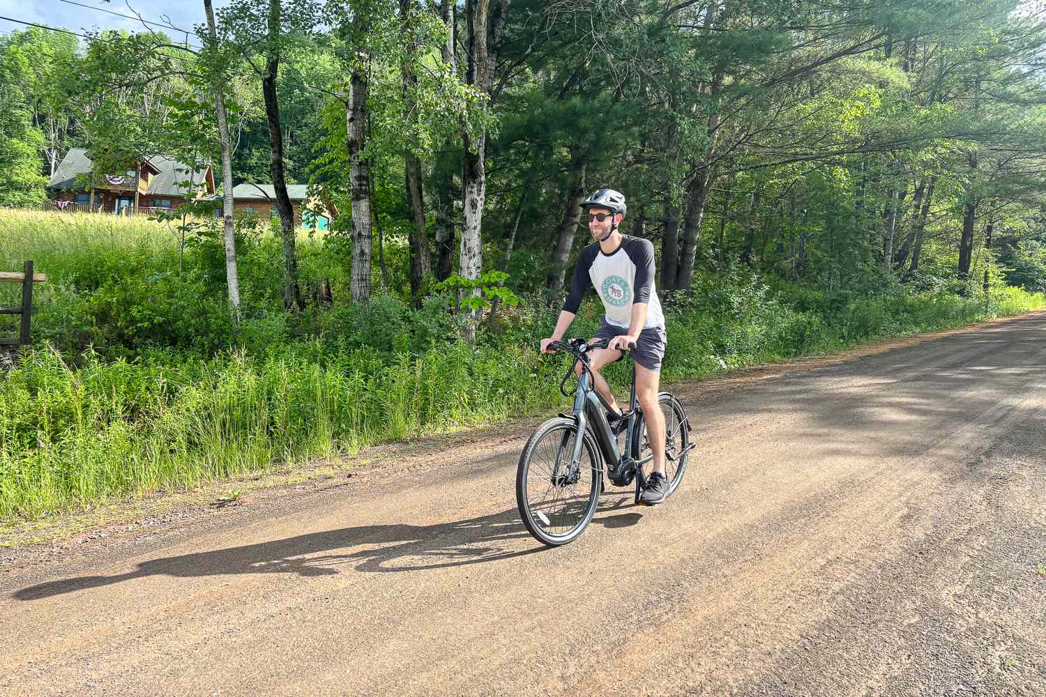 A person riding a Priority e-bike on a quiet rural road, trees and grassland in the background