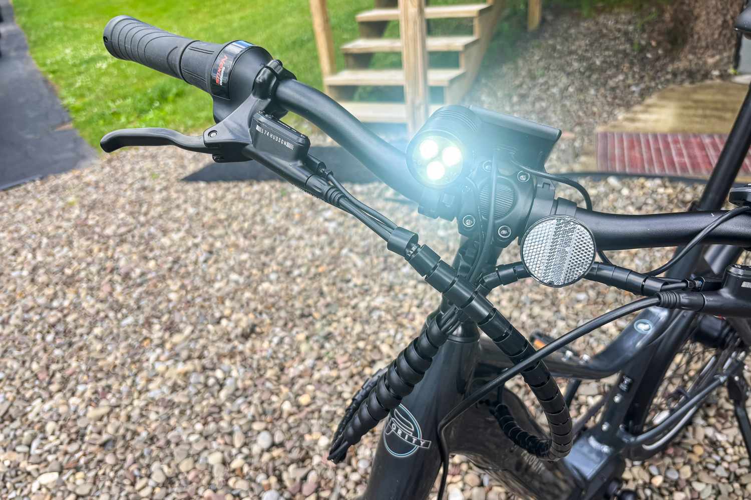The handlebars and brake lever of a Priority electric bike with mounted lights and cables; part of the front frame is visible