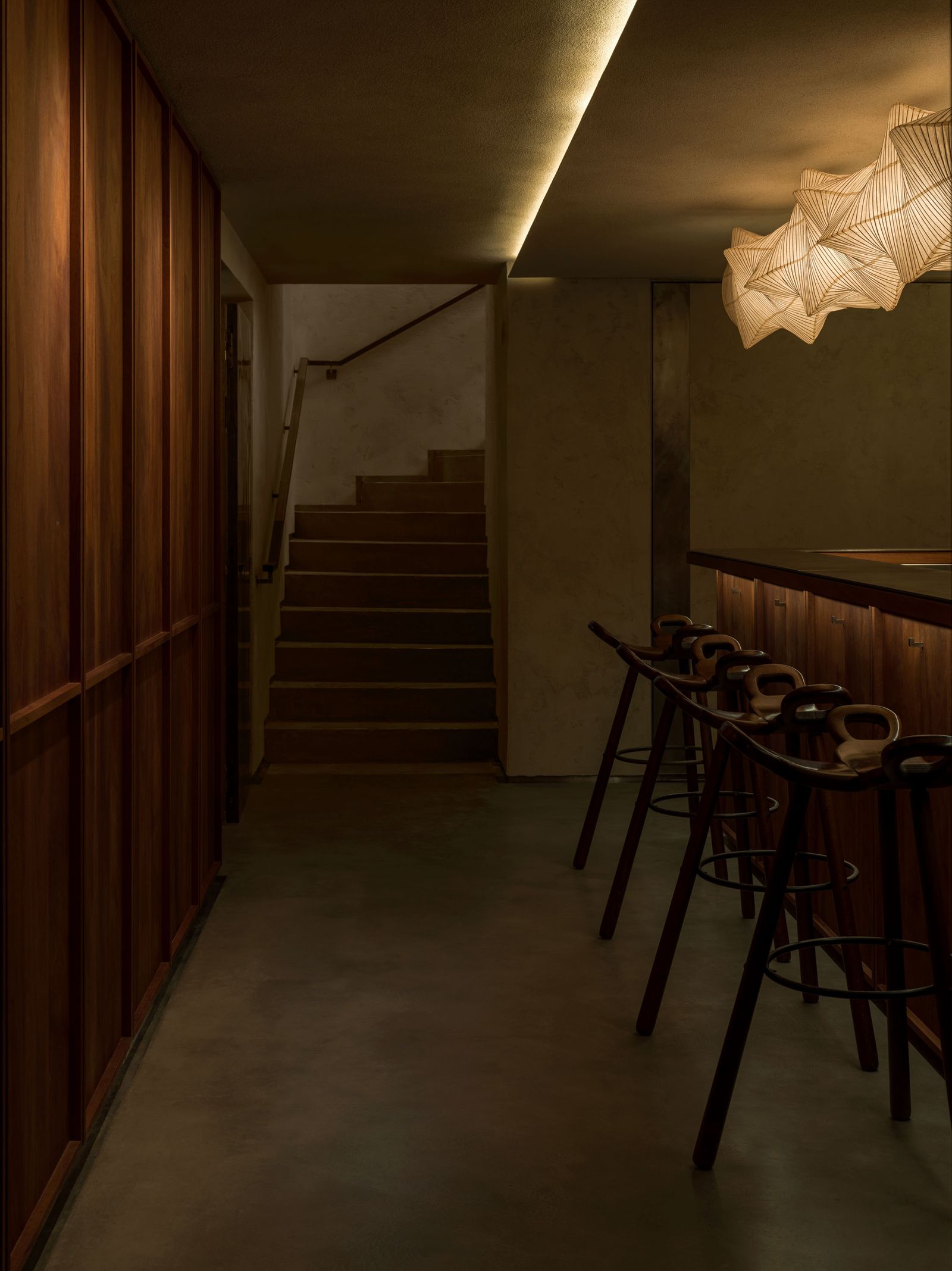 Interior of a dimly lit restaurant with a staircase and bar seating