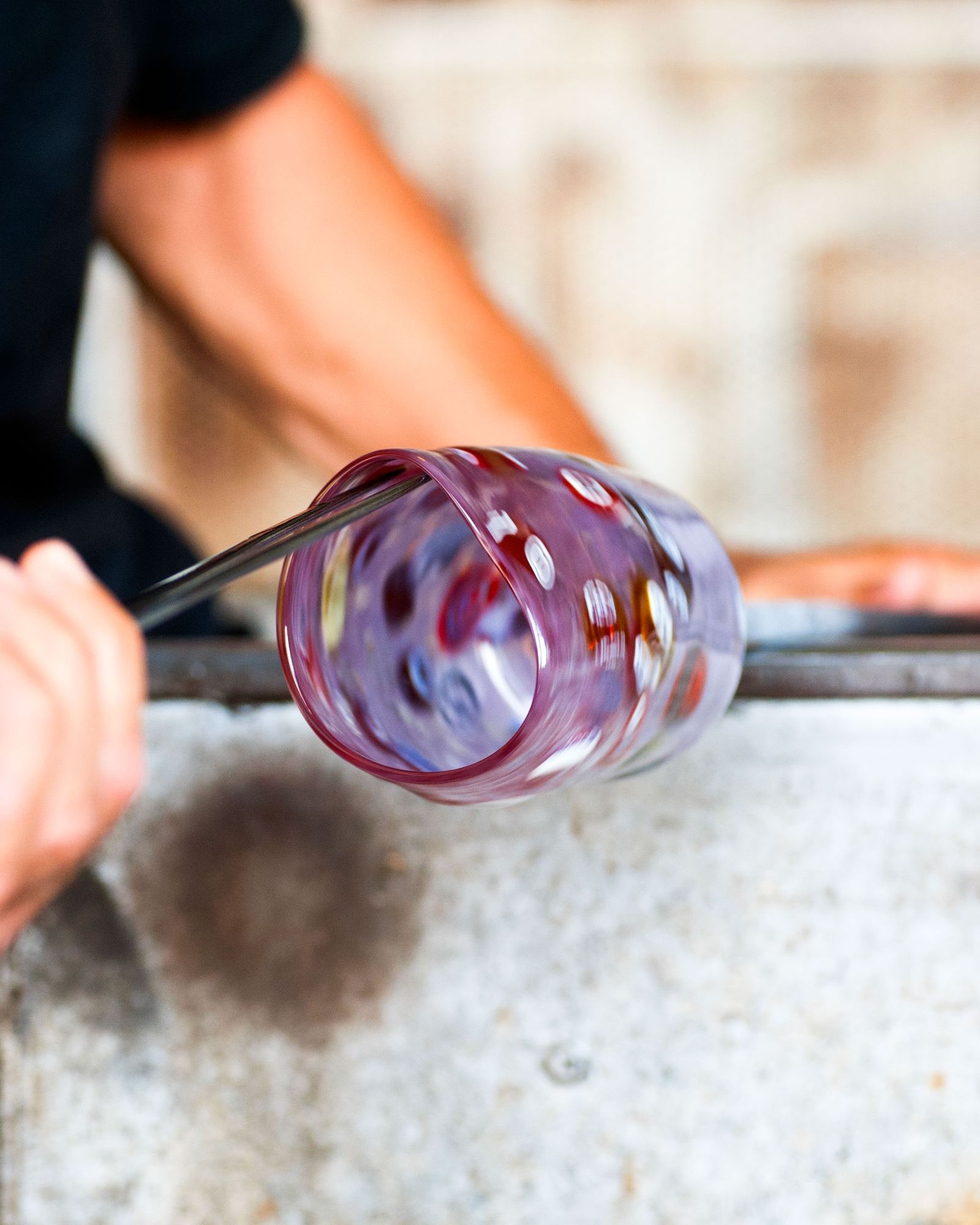 Close up of a glass blower shaping melting glass into a glass by turning it and using a plier