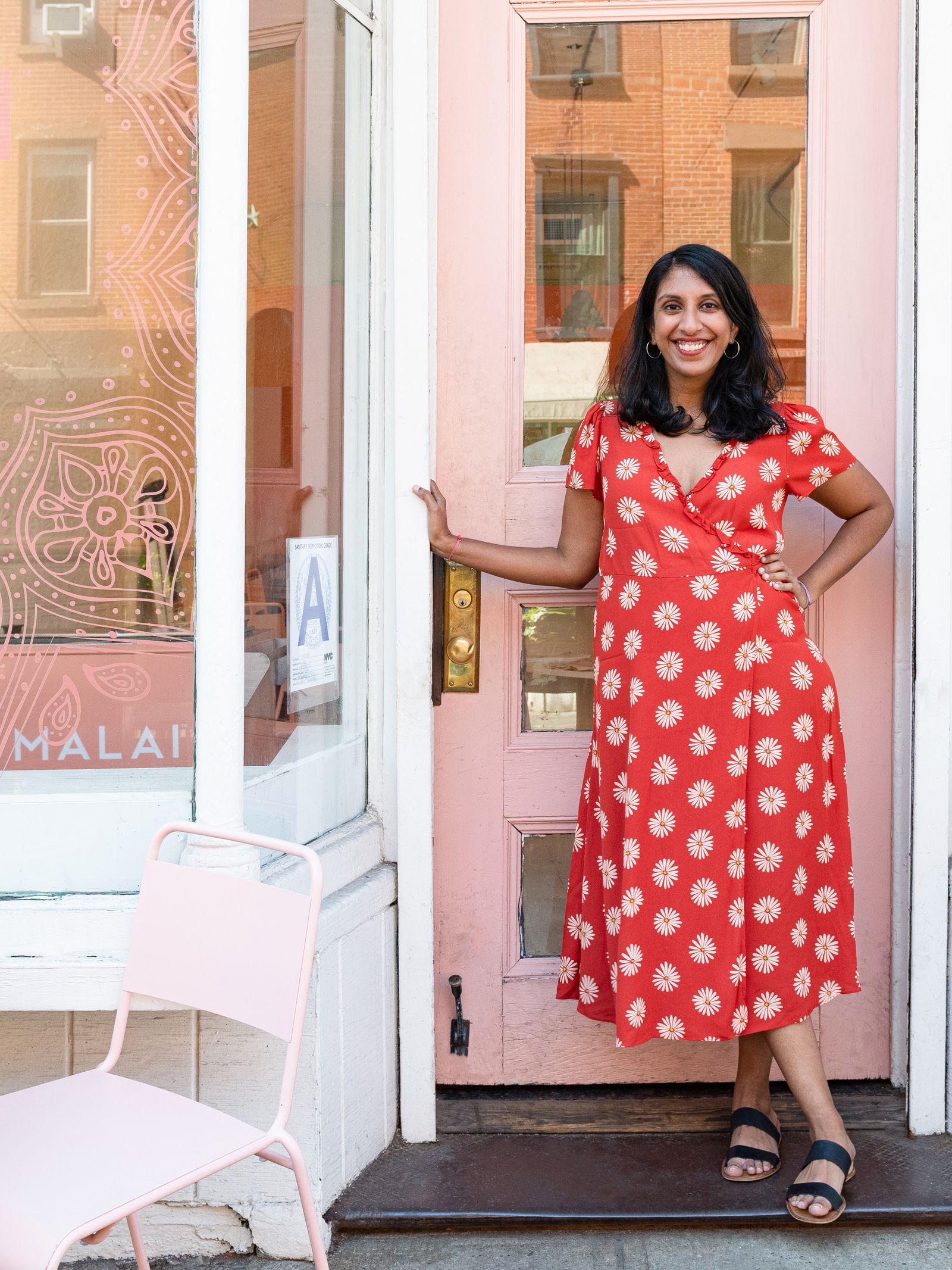 Person wearing a red floral dress smiling and posing outside of the Malai store front