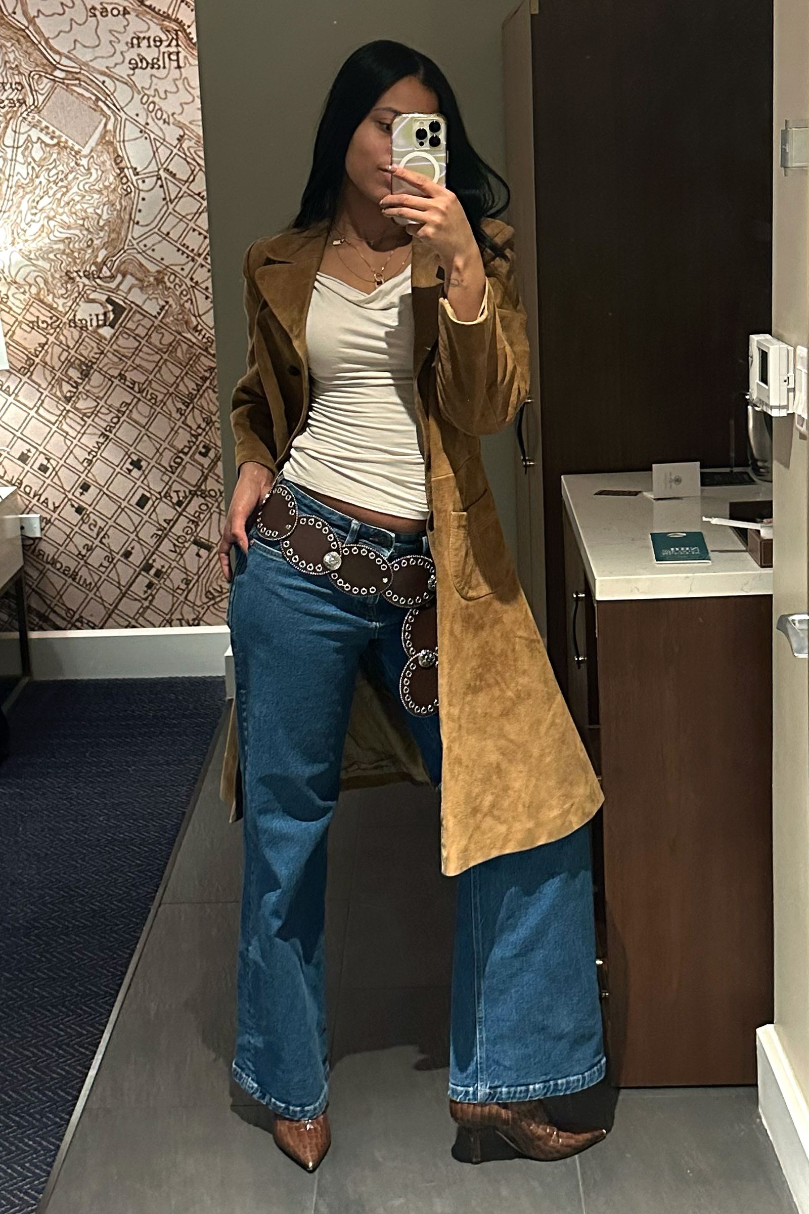 Person taking a selfie while wearing a beige trench coat blue jeans and white shirt