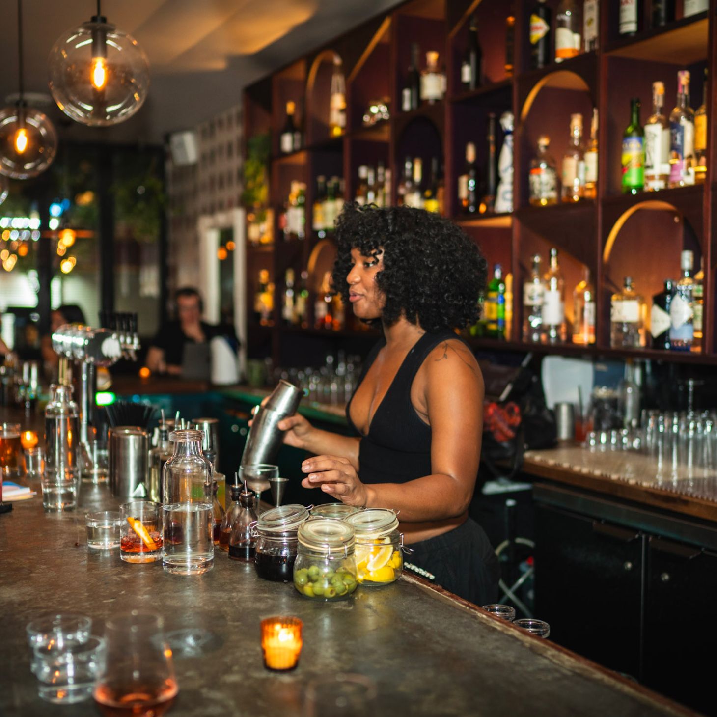 Bartender mixing cocktails behind the bar while talking to guests at Nobody Told Me